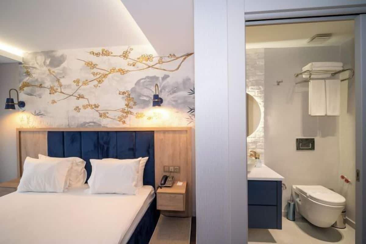 A modern hotel room with a bed, bedside table, and a bathroom with a toilet and sink.
