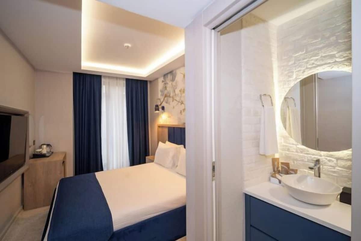 A hotel room with a bed, a bedside table, a TV, a bathroom with a sink and mirror.