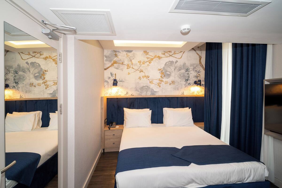 A hotel room with a large bed, a nightstand, a mirror, and a wall with floral wallpaper.