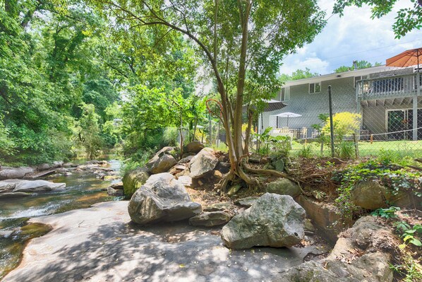 A serene riverside setting with a stone pathway, large rocks, and lush greenery.