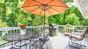 Une terrasse avec une table ronde, des chaises, un barbecue et un parasol.