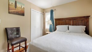 Une chambre à coucher avec un lit, une chaise, un tableau au mur et une fenêtre avec des rideaux.