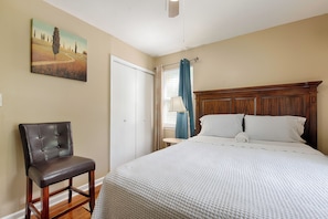 Un dormitorio con una cama, una silla, un cuadro en la pared y un ventanal con cortinas.