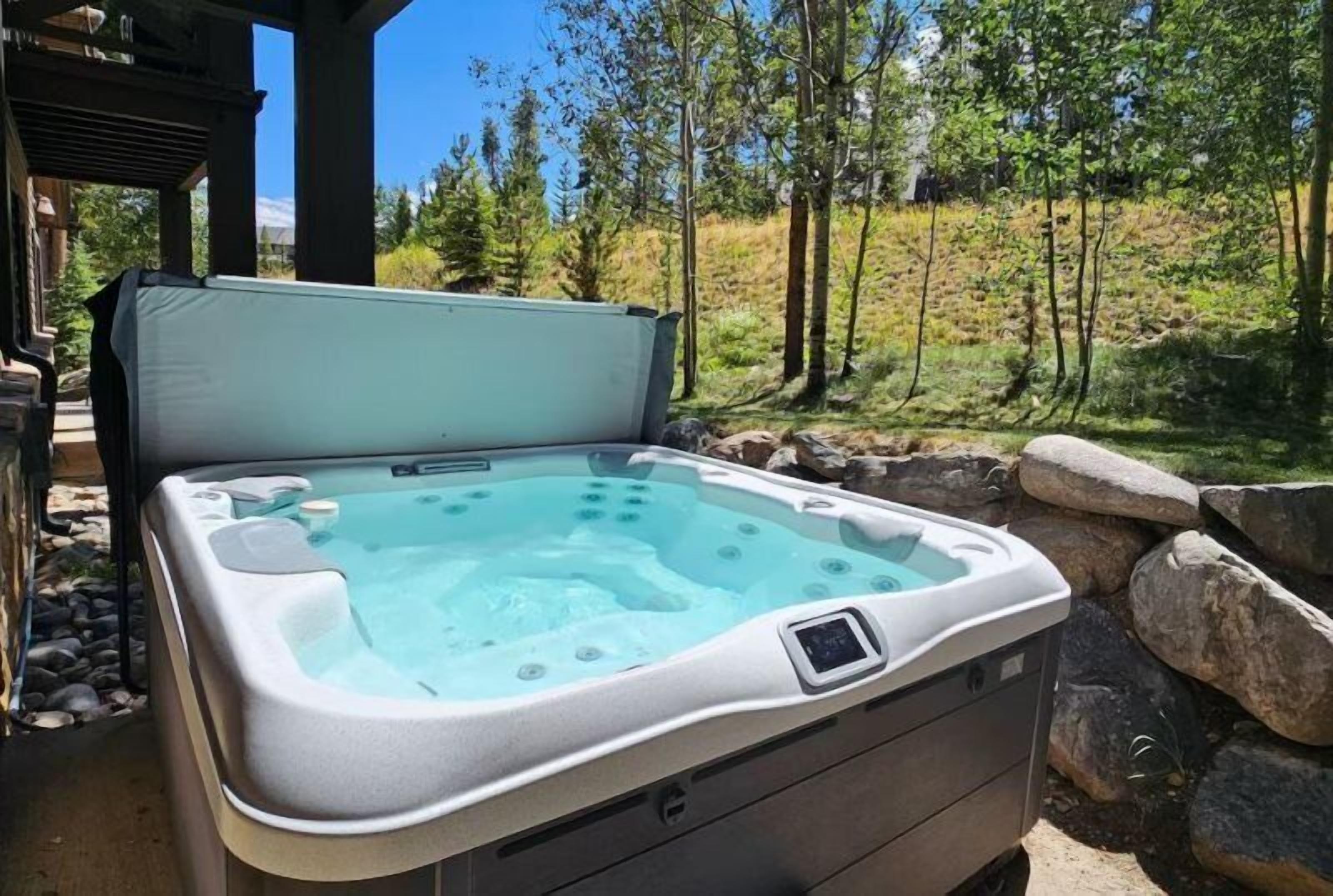 Un jacuzzi con panel de control, situado en un entorno natural al aire libre con árboles y rocas.