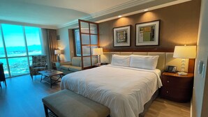 A hotel room with a large bed, a desk, a chair, a small table, and a view of the city. - Renovated Luxury Studio Suite in Tower 3, New Luxury Suite Tower 3 (Paradise)