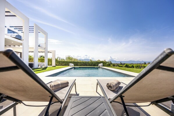 A pool with lounge chairs, a modern building, and a view of mountains.