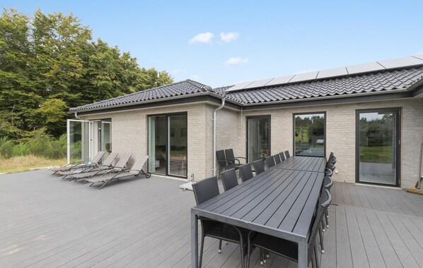A modern house with a patio area featuring a dining table and chairs, large sliding glass doors, and a covered deck. - 6 bedroom nice home in Glesborg (Glesborg)