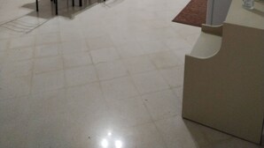 Een kleine, eenvoudig ingerichte kamer met een bed, een tafel en stoelen. Er is een deur naar een andere kamer, een klein plankje en een prullenbak.