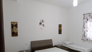 Een slaapkamer met een groot bed, een kleiner bed, een nachtkastje, een lamp en twee decoraties aan de muur.