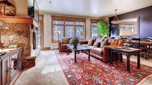 A spacious living room with a stone fireplace, leather sofas, a red patterned rug, and large windows. - Ski in, ski out 3 Bedroom at Lone Eagle in River Run (Keystone)