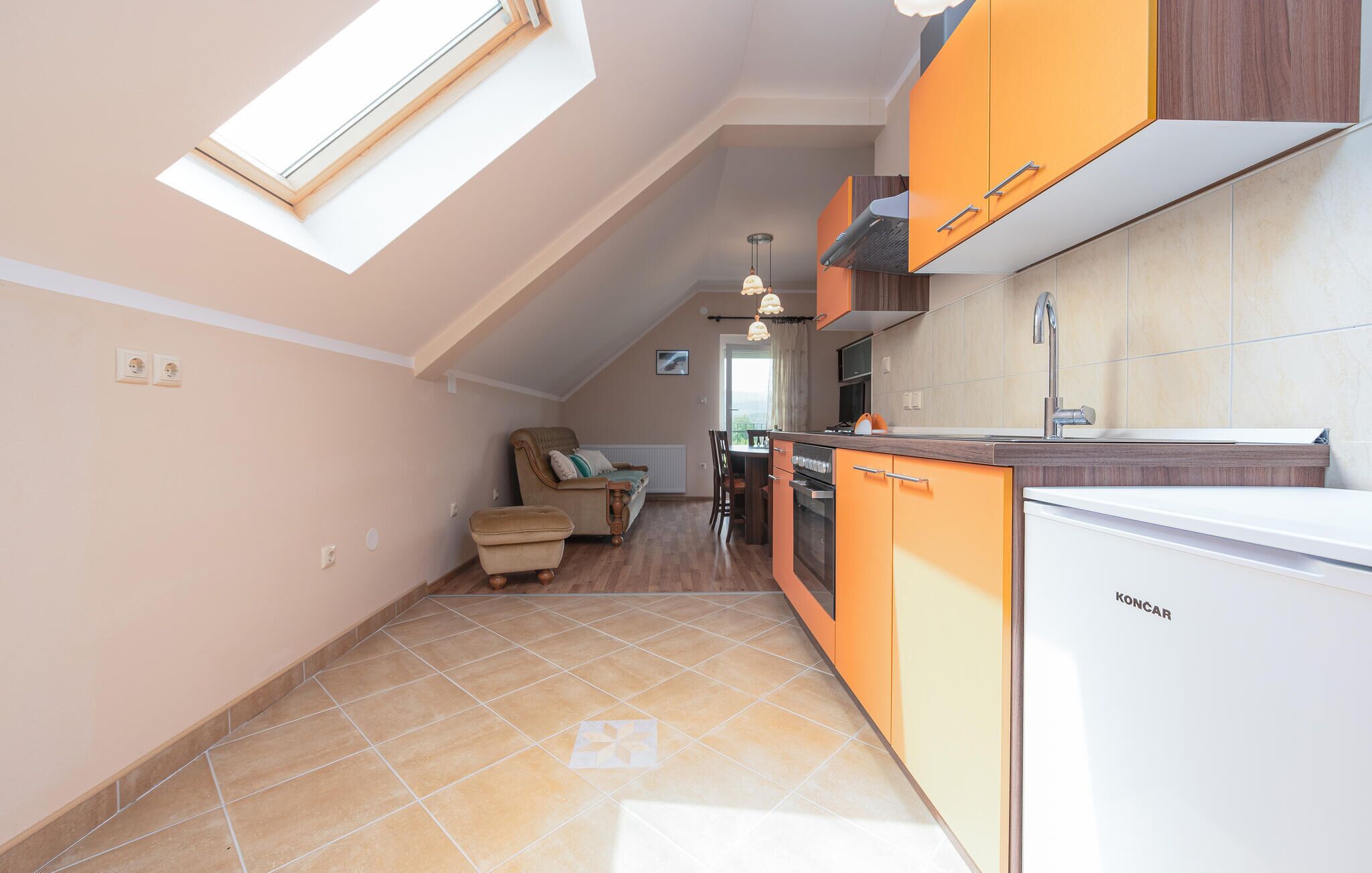 A compact kitchen with orange cabinets, a white refrigerator, and a dining area with a sofa and table.