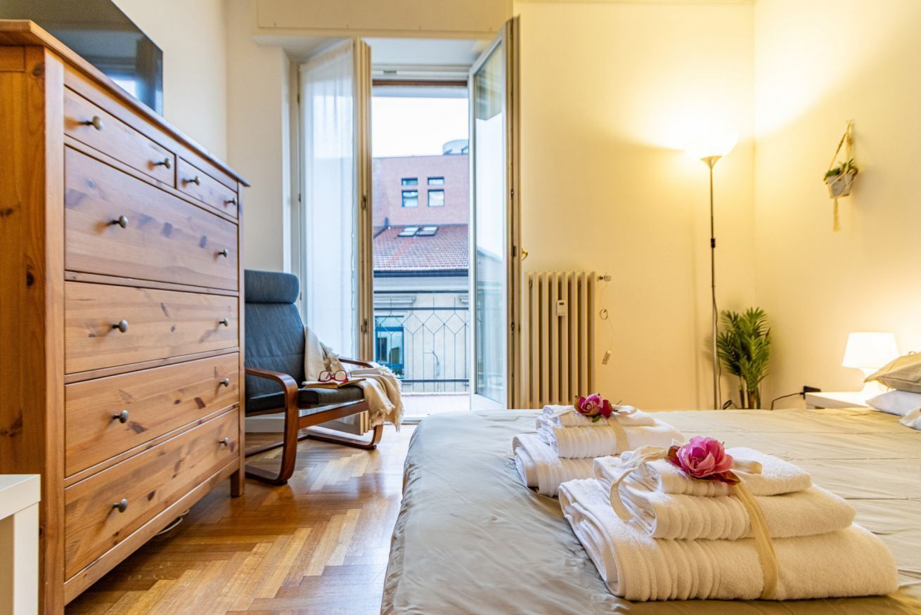 Ett hotellrum med en byrå i trä, en stol, en säng med prydligt hopvikta handdukar, ett element och utsikt över omgivningen.
