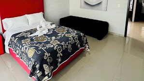 Un dormitorio moderno con un cabecero rojo, una colcha estampada, una almohada blanca, un banco negro y una obra de arte colgada en la pared.