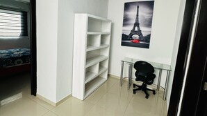 Una habitación con una cama, un estante blanco, un escritorio de cristal con una silla y un cartel de la Torre Eiffel.
