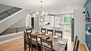 Una cocina moderna con armarios blancos, un comedor con sillas de madera y una escalera que sube a un nivel superior.