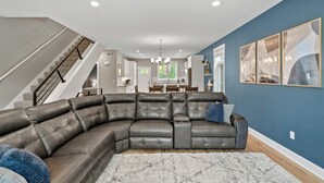 Una sala de estar moderna con un sofá modular, una escalera y un comedor al fondo.