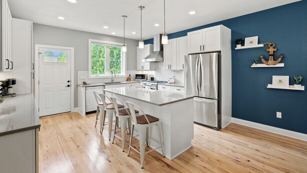 Una cocina moderna con una isla central, taburetes de bar, electrodomésticos de acero inoxidable y una pared azul de acento.