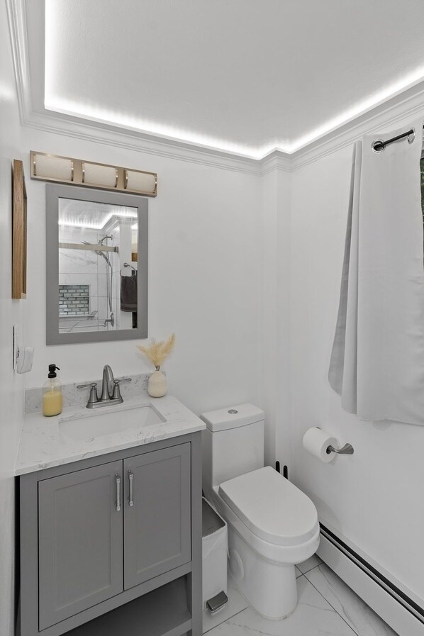 A modern bathroom with a white sink, a mirror, a toilet, and a shower curtain.