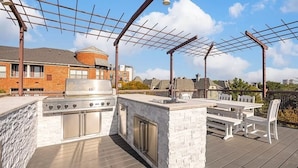 An outdoor kitchen with a grill, sink, and seating area on a deck. - Dallas Townhouse with rooftop (Dallas)