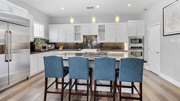 A modern kitchen with white cabinets, a central island with bar stools, and pendant lighting. - Dallas Townhouse with rooftop (Dallas)