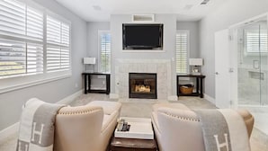 A living room with a fireplace, two armchairs, a coffee table, and a flat-screen TV mounted above the fireplace. - Dallas Townhouse with rooftop (Dallas)