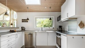 A modern kitchen with white cabinets, a dishwasher, a coffee maker, and a window with a view of trees. - Lovely home in Glesborg with sauna (Glesborg)
