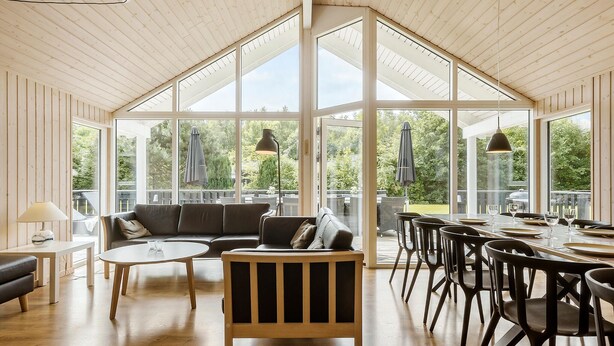A spacious room with a high ceiling, large windows, a sofa, a dining table with chairs, and a lamp. - Lovely home in Glesborg with sauna (Glesborg)