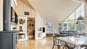 A spacious living area with a large window, a fireplace, and a dining table with chairs. - Lovely home in Glesborg with sauna (Glesborg)