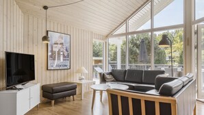 A modern living room with a large window, a sofa, a TV, and a small table. - Lovely home in Glesborg with sauna (Glesborg)