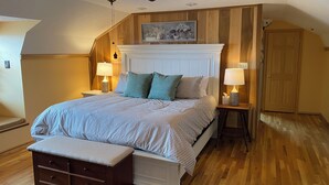 A bedroom with a large bed, two bedside tables with lamps, a ceiling fan, a wooden bench, and a door. - Stunning, Mtn-Top, Lakeview Cabin on Private 8 acres (Butler)