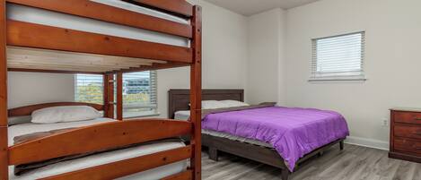 Un dormitorio con dos literas y una cama individual, suelo de madera, ventilador de techo y una ventana con persianas.