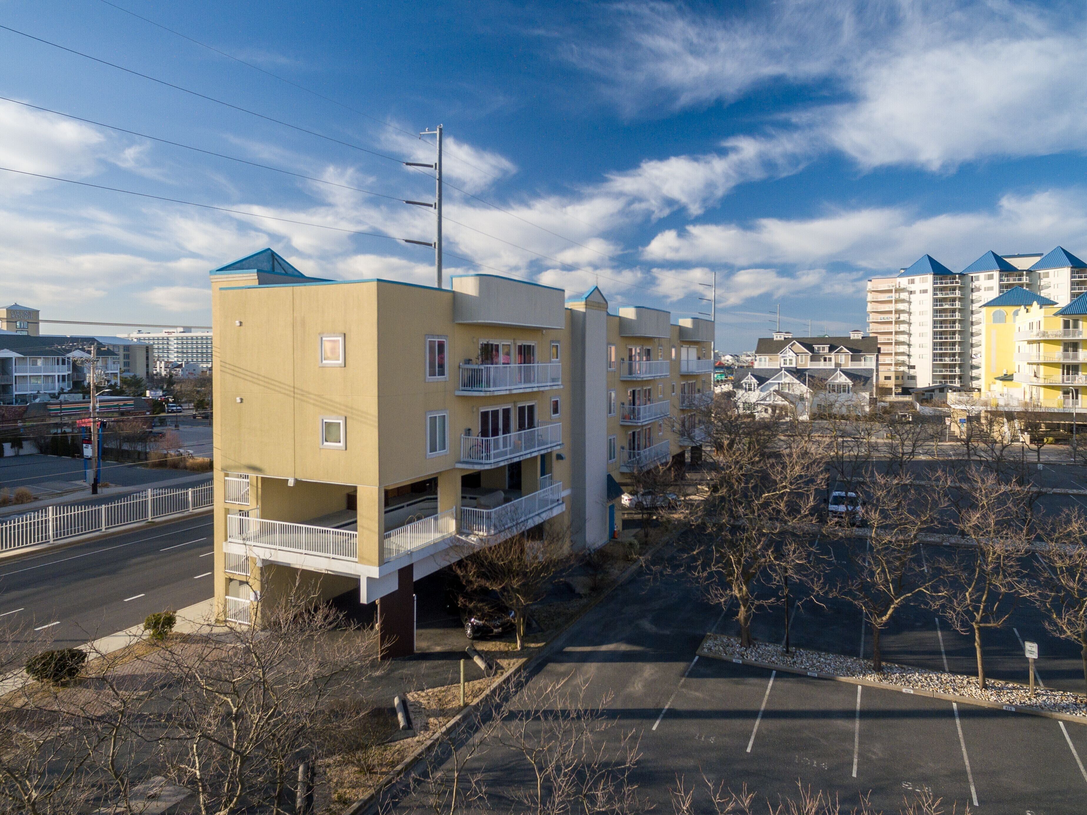 A multi-story residential building with balconies, a parking lot, and a clear sky.