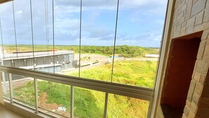 Vista desde una ventana con marco de metal y pared de ladrillo, sobre un paisaje verde con carretera y edificios.