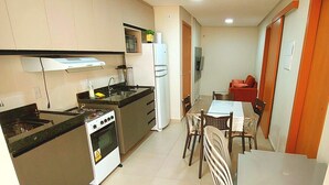 Una cocina compacta con estufa, pileta y refrigerador, un comedor con sillas y mesa, y una pequeña sala de estar con sofá.
