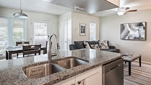 A modern kitchen with granite countertops, a stainless steel sink, and a dishwasher. There is a dining area with a table and chairs, and a ceiling fan above. - Newly Renovated Unit: Contemporary Interiors, Minutes from Fine Dining & Wold Class Skiing! (Park City)