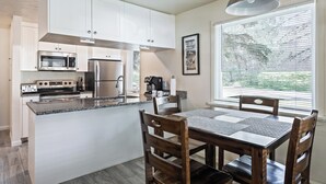 A modern kitchen with white cabinets, stainless steel appliances, and a dining area with wooden chairs and a table. - Newly Renovated Unit: Contemporary Interiors, Minutes from Fine Dining & Wold Class Skiing! (Park City)