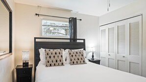 A neatly made bed with patterned pillows, a bedside table with a lamp, and a window with a curtain. - Newly Renovated Unit: Contemporary Interiors, Minutes from Fine Dining & Wold Class Skiing! (Park City)