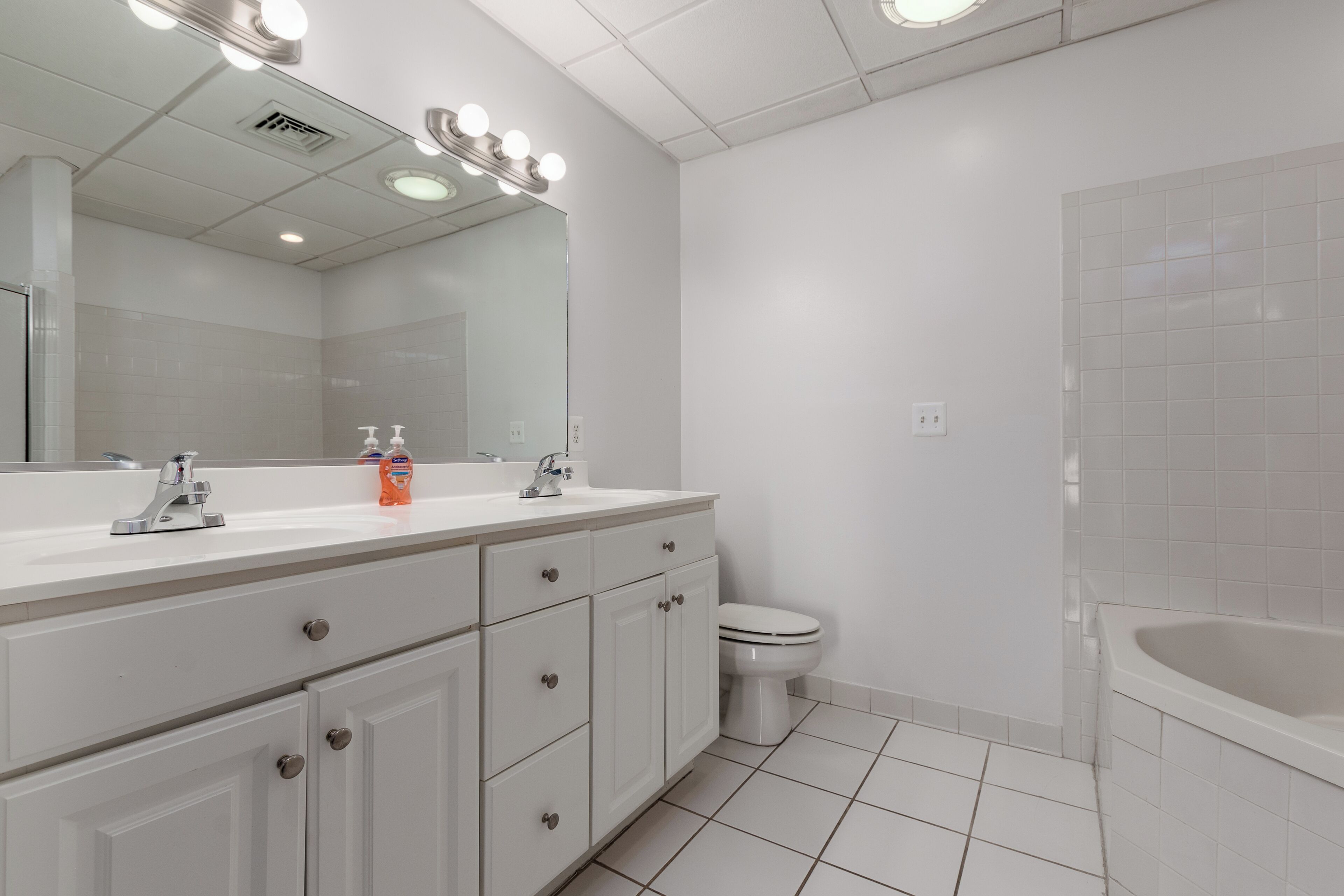 Een moderne badkamer met een wit wastafelmeubel, een grote spiegel met verlichting, een toilet en een bad.