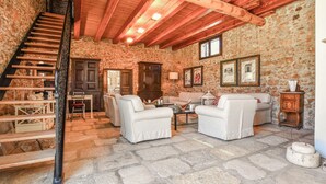 Um quarto com paredes de pedra, uma escada, dois sofás, uma mesa e quadros nas paredes.