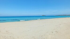 Uma praia com águas azul-claras, uma faixa de areia e uma pequena ilha ao longe.
