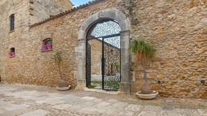 Um edifício de pedra com um grande arco, vasos de plantas e um pátio de paralelepípedos.
