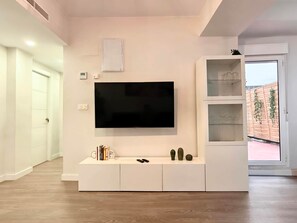 A modern living room with a flat-screen TV mounted on the wall, a white entertainment unit with books and decorative items, and a wooden floor.