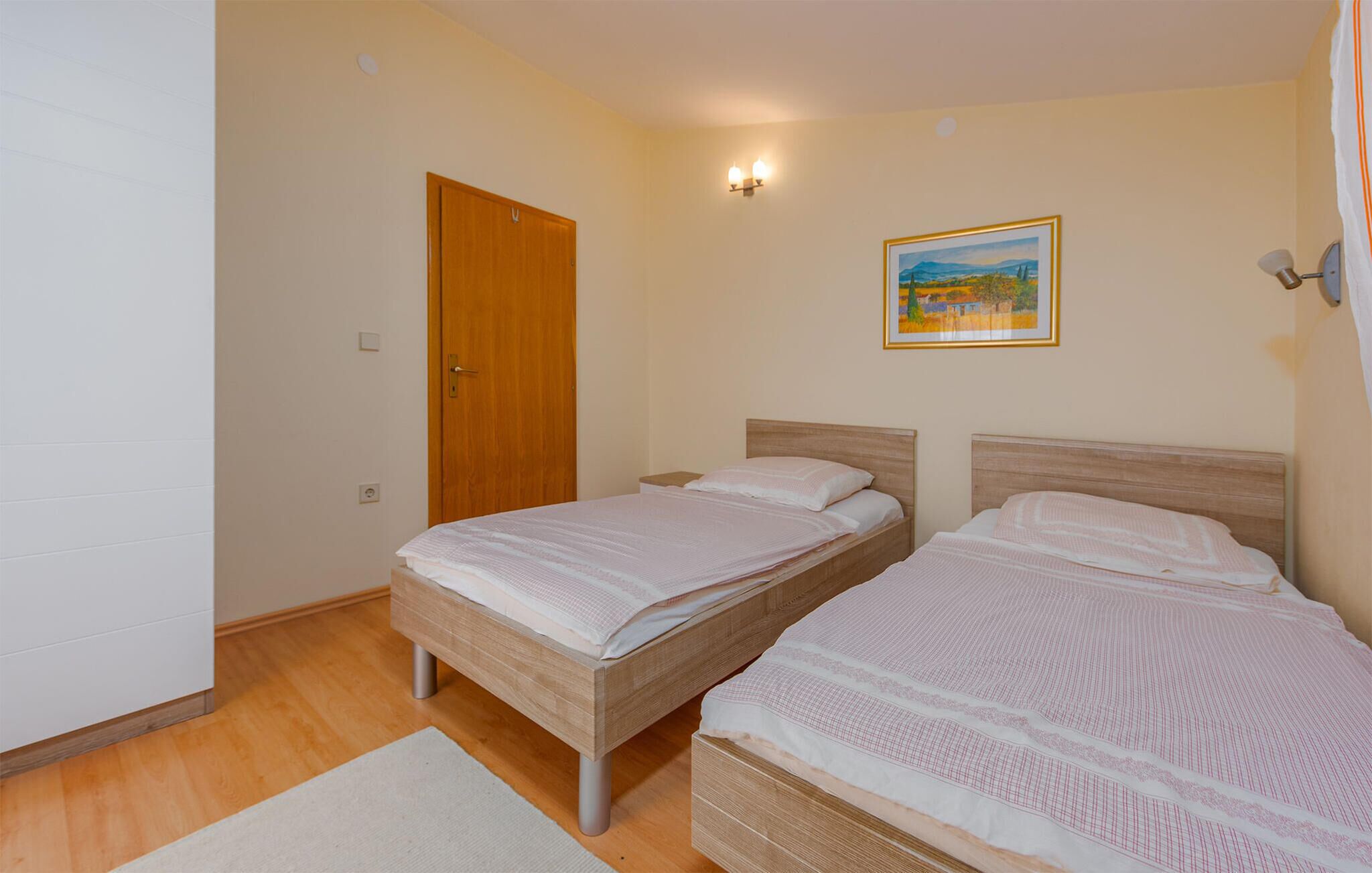 Une chambre avec deux lits, une porte en bois, un tableau au mur et une table de chevet.