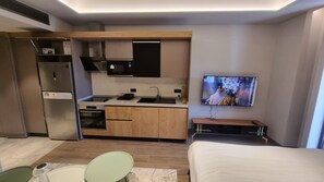 Habitación de hotel compacta con kitchenette, cama, televisión y un pequeño rincón de descanso.