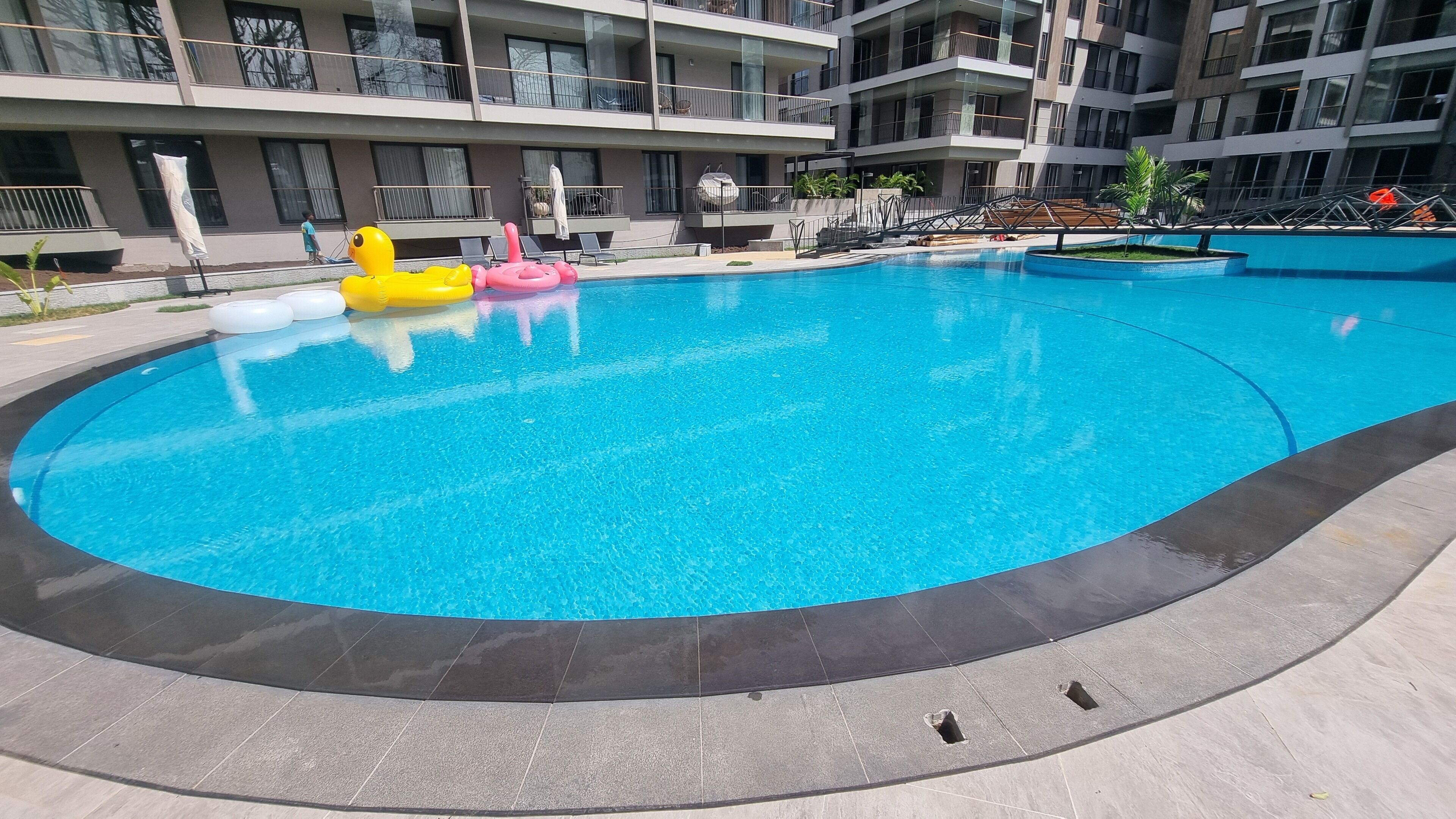 A swimming pool with inflatable toys, surrounded by a modern building with balconies.
