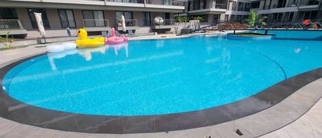 A swimming pool with inflatable toys, surrounded by a modern building with balconies.