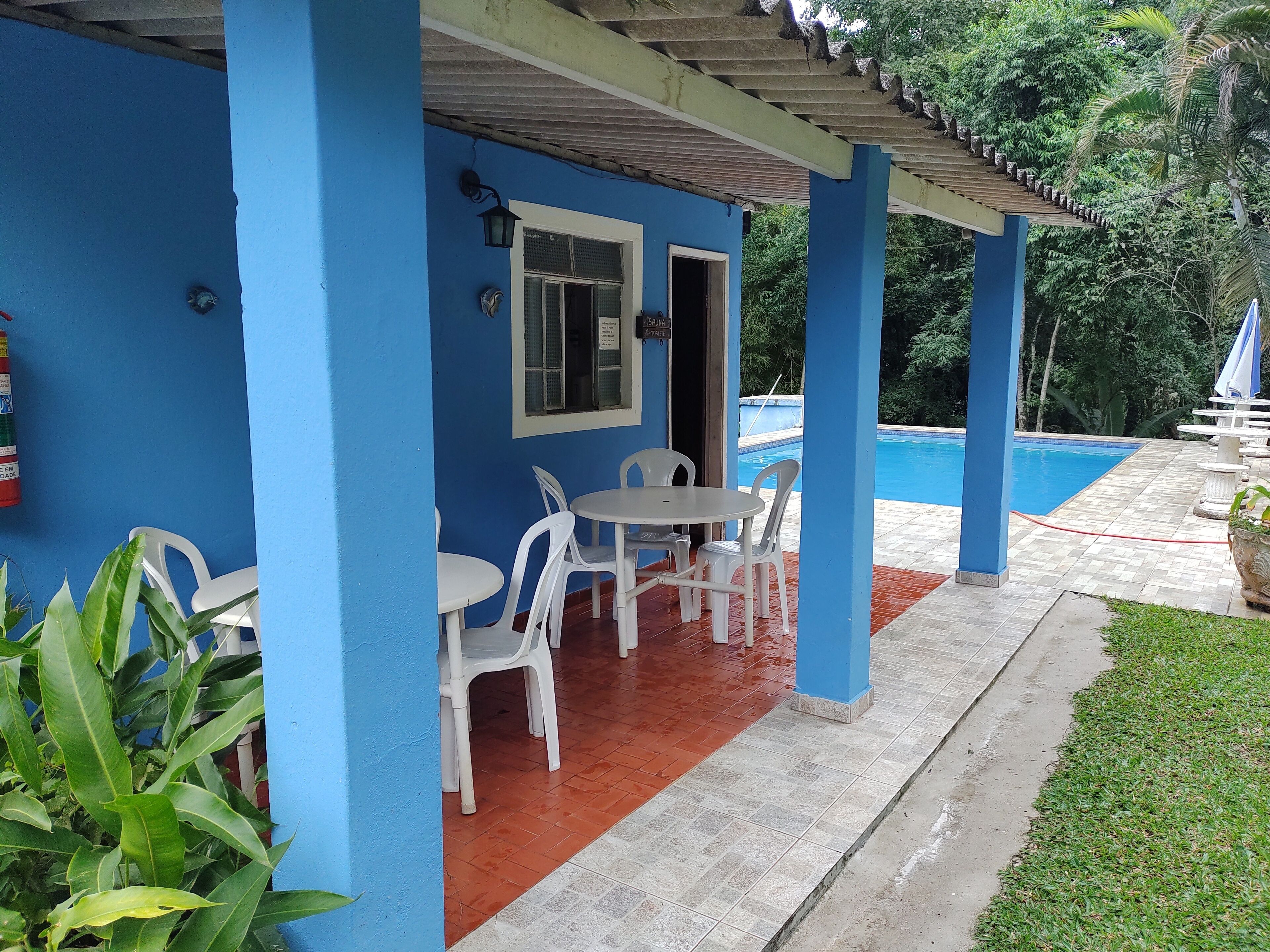 A blue building with a covered patio area featuring white plastic chairs and a small table.
