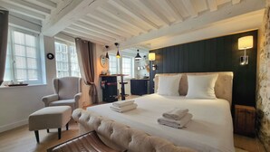 Una habitación de hotel con una cama grande, una silla, un banco, un escritorio y un espejo.