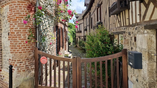 Un estrecho callejón con edificios tradicionales de entramado de madera, un portón de madera y flores en flor.