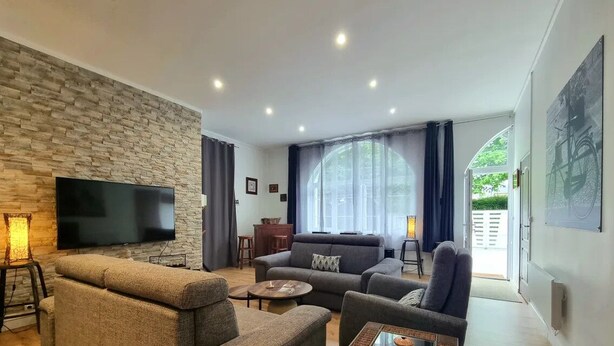 A modern living room with a stone wall, a flat-screen TV, a sofa, a coffee table, and a lamp.